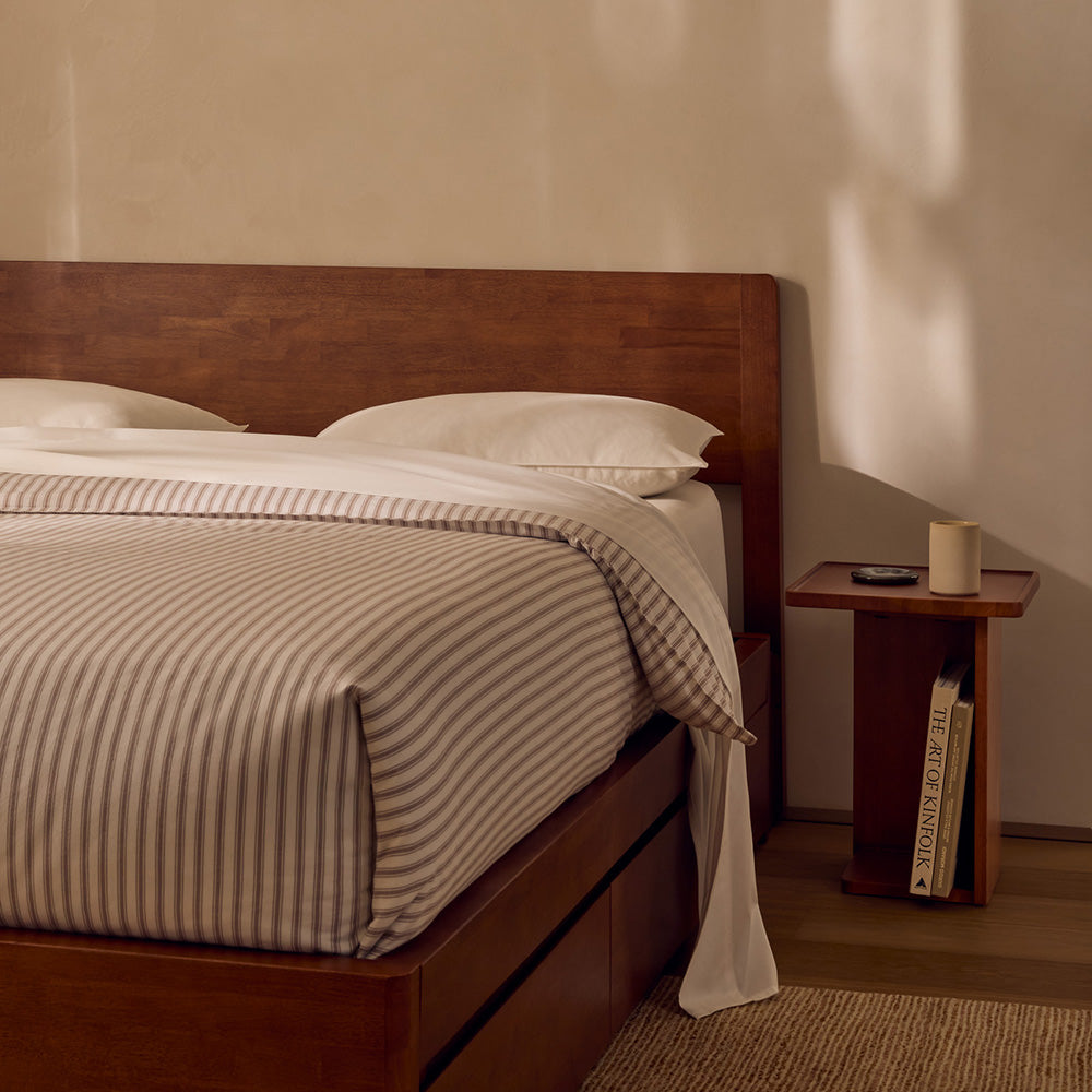 Bedroom with wooden bed and side table, featuring striped bedding and a candle.